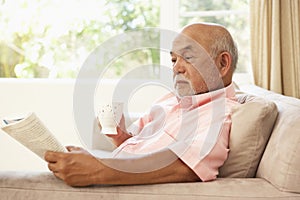 Senior Man Reading Book With Drink At Home