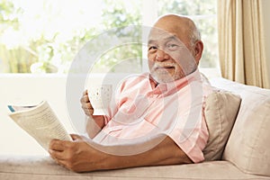 Senior Man Reading Book With Drink At Home