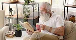 Senior man reading a book and drinking coffee at home