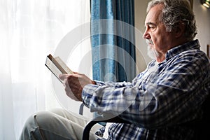 senior man reading book while sitting on wheelchair in nursing home photo