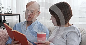 Senior man reading a book to his wife drinking coffee