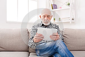 Senior man reading news on digital tablet