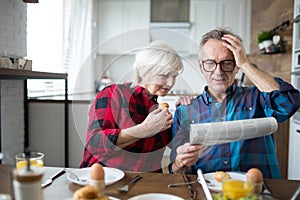 Senior man reading newspaper during breakfast with wife