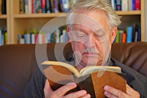 Senior man reads in front of bookcase