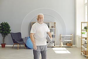 Senior man ready for active fitness training holding sports mat and looking at camera