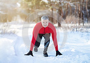 Senior man ready to jog on country road with snow on cold winter day. Active lifestyle and acclimation concept