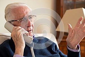 Unhappy Senior Man Receiving Unwanted Telephone Call At Home photo