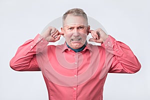 Senior man in red shirt plugging ears with fingers