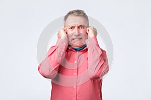 Senior man in red shirt plugging ears with fingers