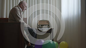 Senior man reflecting alone in a bedroom with colorful balloons and a vintage radio