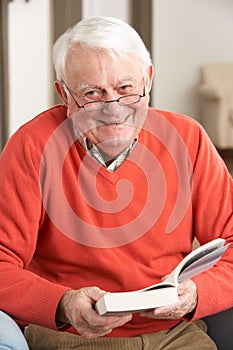 Senior Man Relaxing In Chair At Home Reading Book