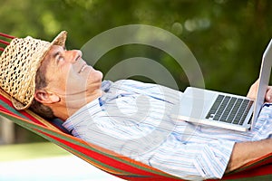 Senior Man Relaxing In Hammock With Laptop