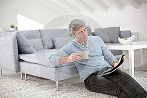 Senior man relaxing at home reading magazine