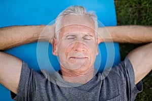 Senior man resting with closed eyes on mat at park