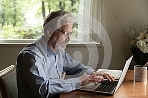 Senior man retiree wearing glasses working browsing news on laptop