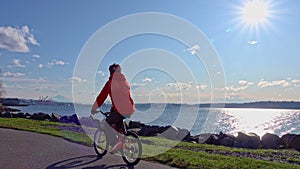 Senior man riding bike on Seattle waterfront trail with bright sun behind