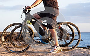 Senior man riding his bici on the cliffs. Horizon over sea at sunset light. Two electric bicycles with battery and engine. One photo