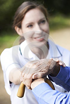 Senior Man's Hands Resting On Walking Stick With Care Worker In