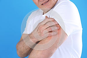 Senior man scratching arm on color background, closeup