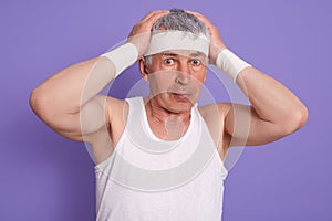 Senior man scratching his head in confusion, wearing white sleeveless t shirt, touching his head, poses isolated over lilac