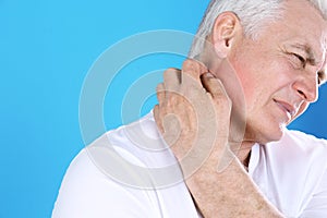 Senior man scratching neck on color background. Allergy symptom