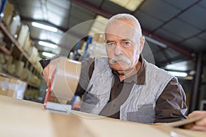 Senior man sealing cardboard box with tape dispenser