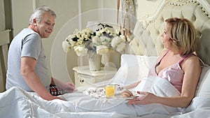 Senior man serving breakfast to woman in bed