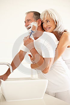 Senior Man Shaving In Bathroom With Wife Watching