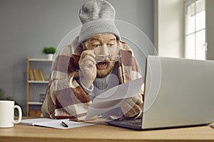 Senior man, shocked by heating costs, sitting in his cold house and holding bill