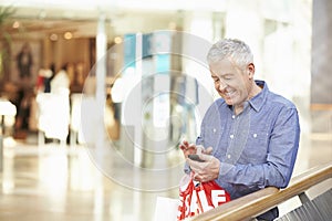 Senior Man In Shopping Mall Using Mobile Phone