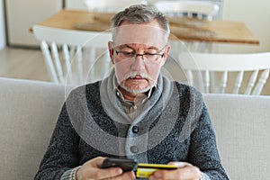 Senior man shopping online holding smartphone paying with credit card Old grandfather buying on Internet enter credit