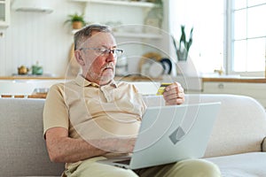 Senior man shopping online using laptop paying with credit card. Old grandfather buying on Internet enter credit card