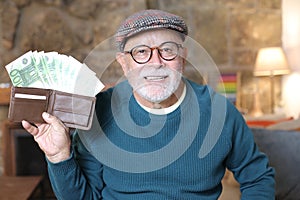 Senior man showing abundance with full wallet at home