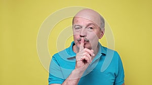 Senior man showing shh gesture, asking for silence or to be quiet.