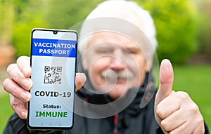 Senior man showing a vaccination passport on a mobile phone, which indicates a vaccination against covid-19. Phone shows a non