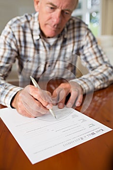 Senior Man Signing Last Will And Testament At Home