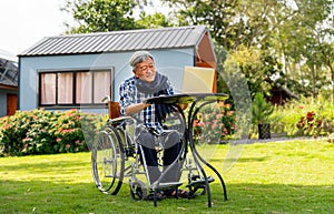 Senior man sit on wheelchair enjoy and relax with laptop outdoor in the garden with warm light