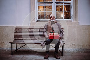 Senior man sitting alone on bench, holding Chrismtas gifts.