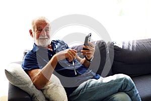 Senior man sitting alone and playing mobile phone at home.