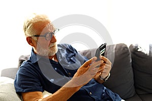 Senior man sitting alone and playing mobile phone at home.