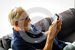 Senior man sitting alone for relaxation and playing game on smart phone in home