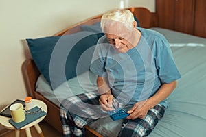 Senior Man Sitting On Bed Taking Medication