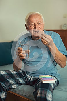 Senior Man Sitting On Bed Taking Medication