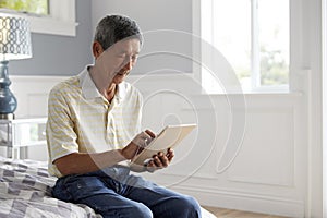 Senior Man Sitting On Bed Using Digital Tablet
