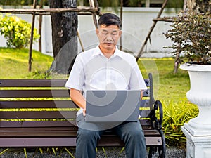 senior man sitting on a bench using a laptop in the park.