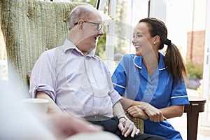 Senior Man Sitting In Chair And Talking With Nurse In Retirement Home