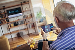 Senior man on a sofa holding remote home control system on a digital tablet