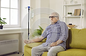 Senior man sitting on couch with iv drip attached on his hand