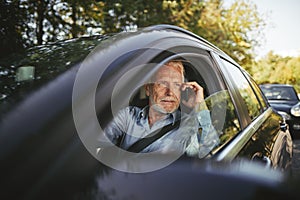Senior man sitting in his car talking on a cellphone