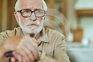 Senior man sitting and holding wooden walking stick at home